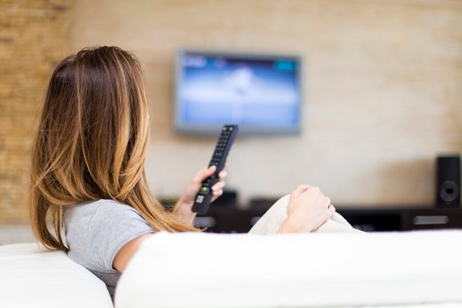 A woman using her smart remote to manage her media control system and setup.
