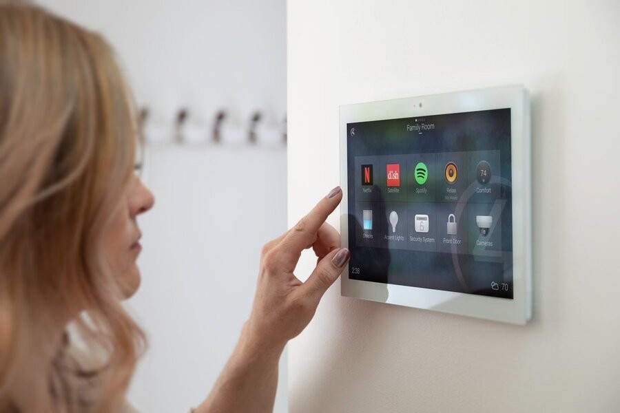 A woman uses a wall touchscreen tablet’s interface to manage her Control4 smart home system