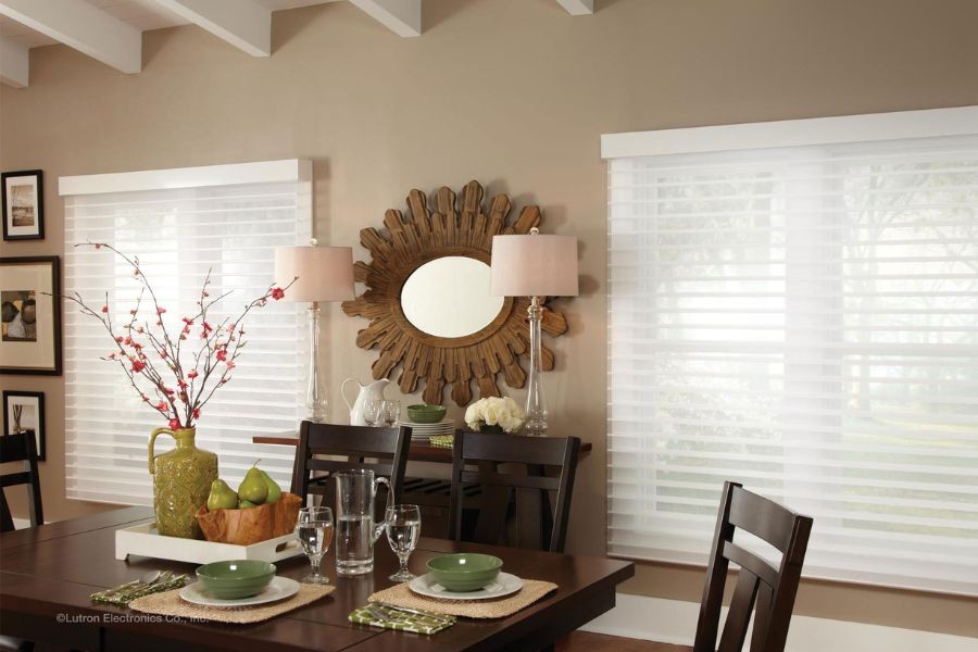 Photo of a kitchen table, two windows with white blinds acting as bookends, a modern but boho-style mirror placed between them. 