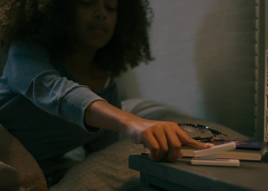 Woman reaching over to her bedside table to adjust the lights using a Lutron pico remote. 