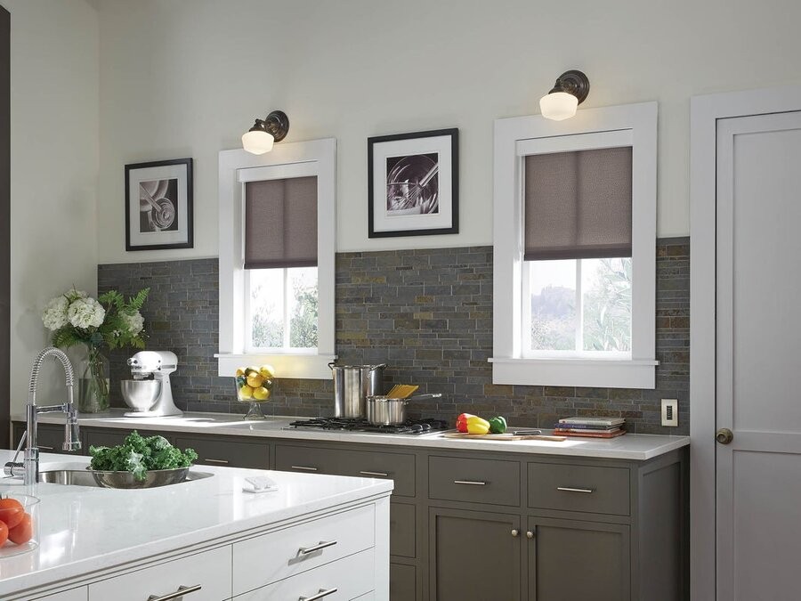 A kitchen space with two windows featuring Lutron motorized shades lowered halfway down, and two Lutron lighting fixtures above each window.