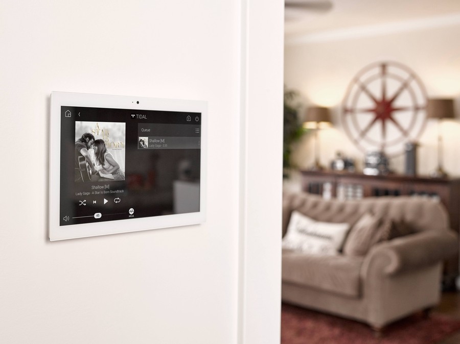 a Control4 touchscreen panel mounted on the wall streaming a song 